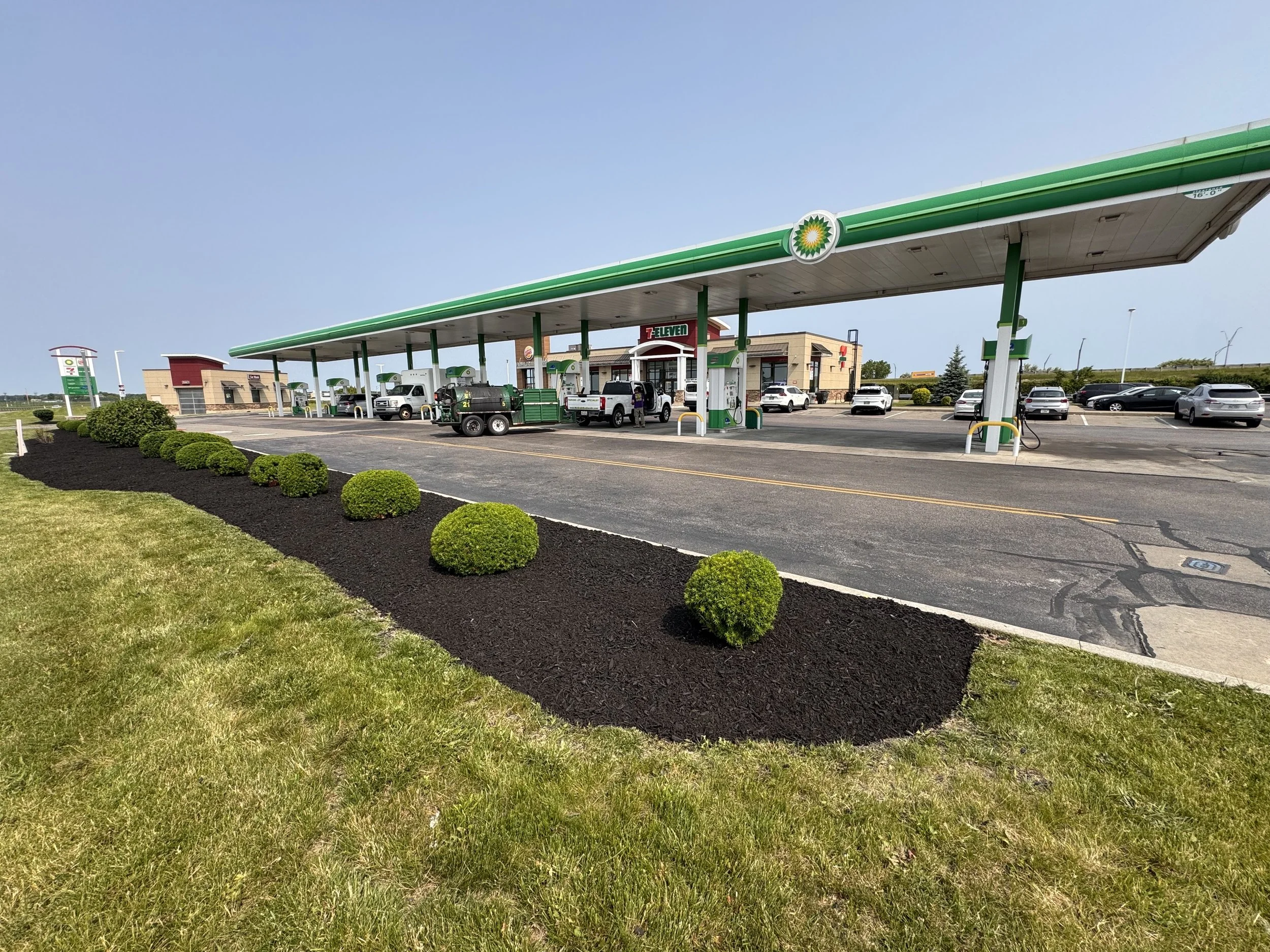 Commercial landscaping at a BP fuel station with a row of shaped shrubs