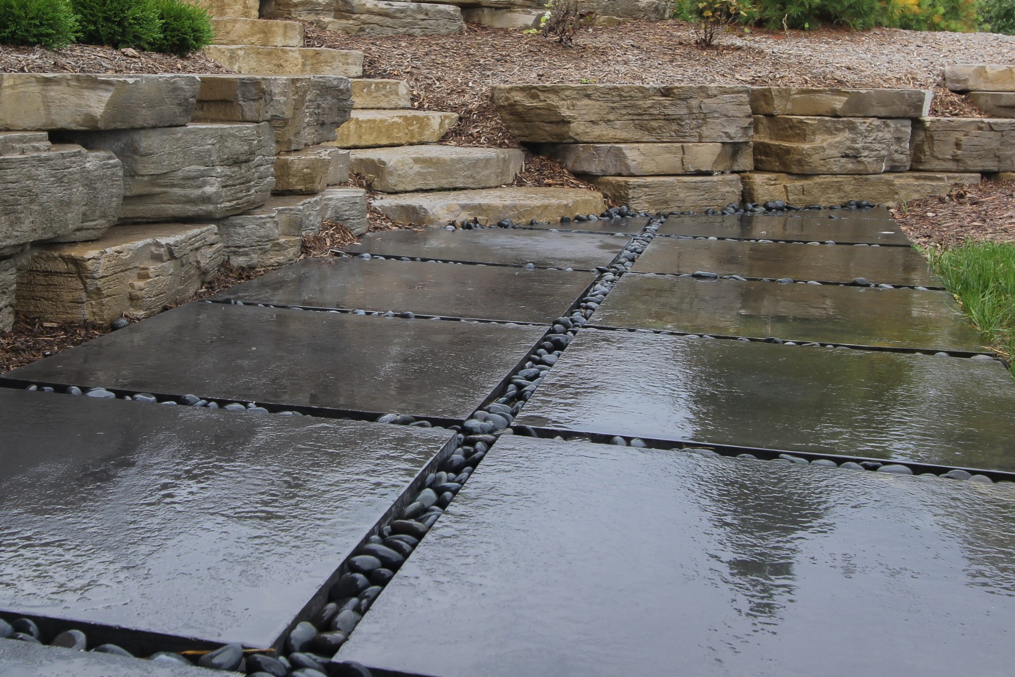 Dark stone tile patio with gravel joints framed by stone walls